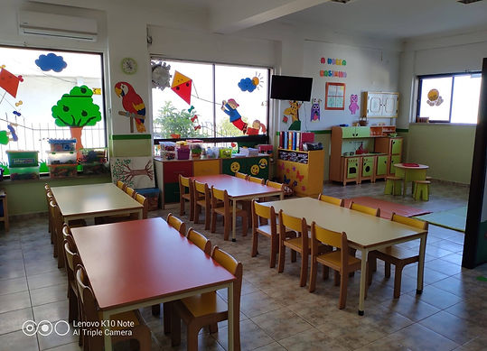 Preschool classroom with colorful tables and chairs, and playful wall decorations.