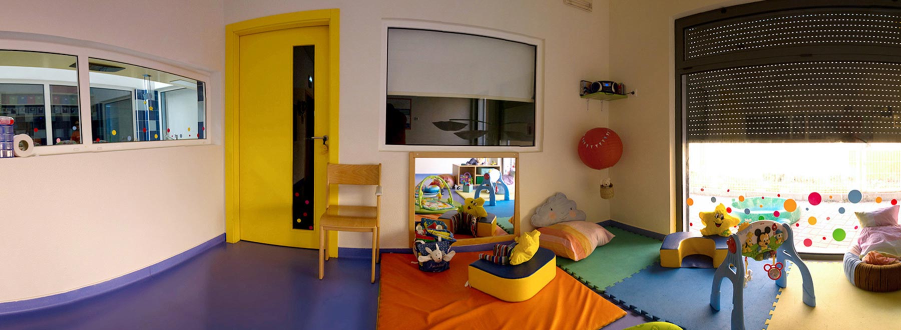 Preschool classroom with colorful mats, toys, and a yellow door
