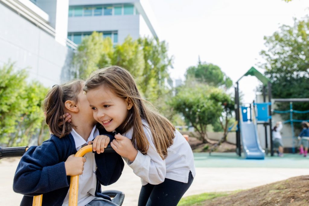 Two preschool girls whispering secrets on playground