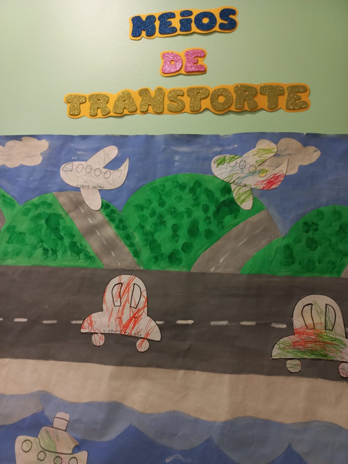 Preschool children's artwork depicting various means of transportation, including airplanes, cars, and a boat. The artwork is displayed on a wall in a classroom.