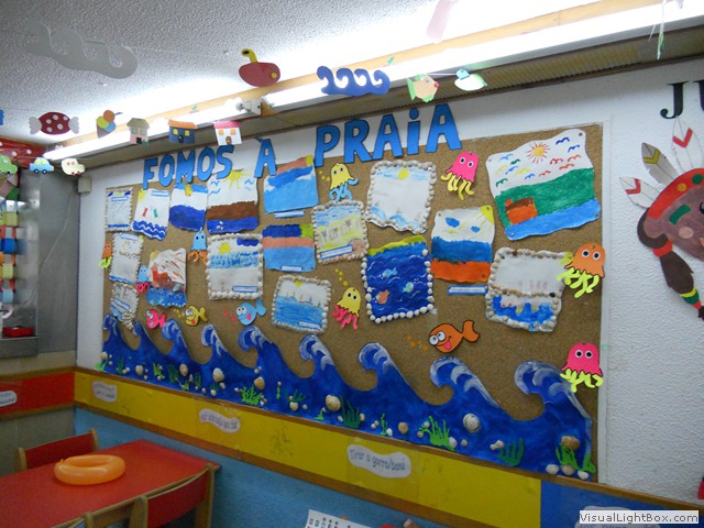 Preschool children's artwork on display, depicting ocean scenes and sea creatures. The artwork is displayed on a corkboard with blue waves and seashells.