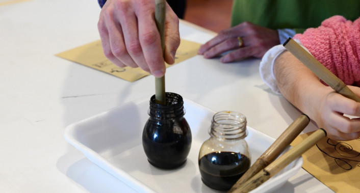 Close-up view of hands using brushes to paint with ink. This image is suitable for a preschool website as it shows a child-friendly art activity.