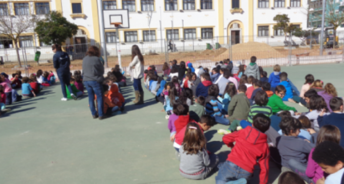 Preschool children sitting on the ground in a large group, possibly during an outdoor assembly or activity.