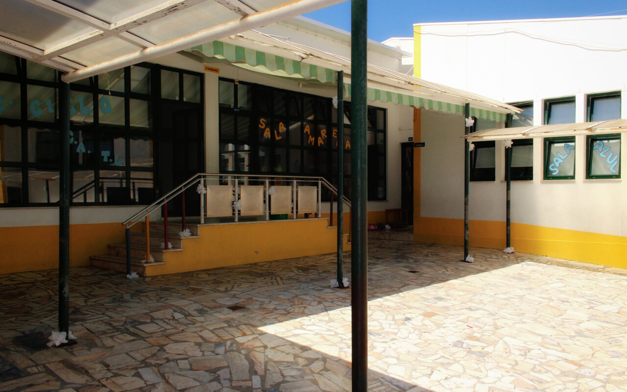 Exterior view of A Nossa Creche preschool, showing a paved courtyard and building entrance.