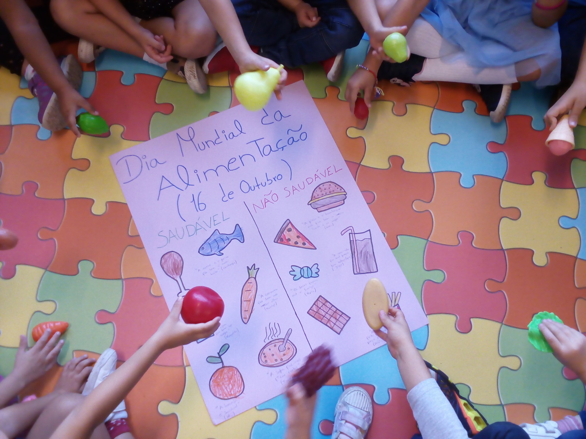 Preschool children participate in a healthy eating lesson, holding colorful food models and surrounding an educational chart.