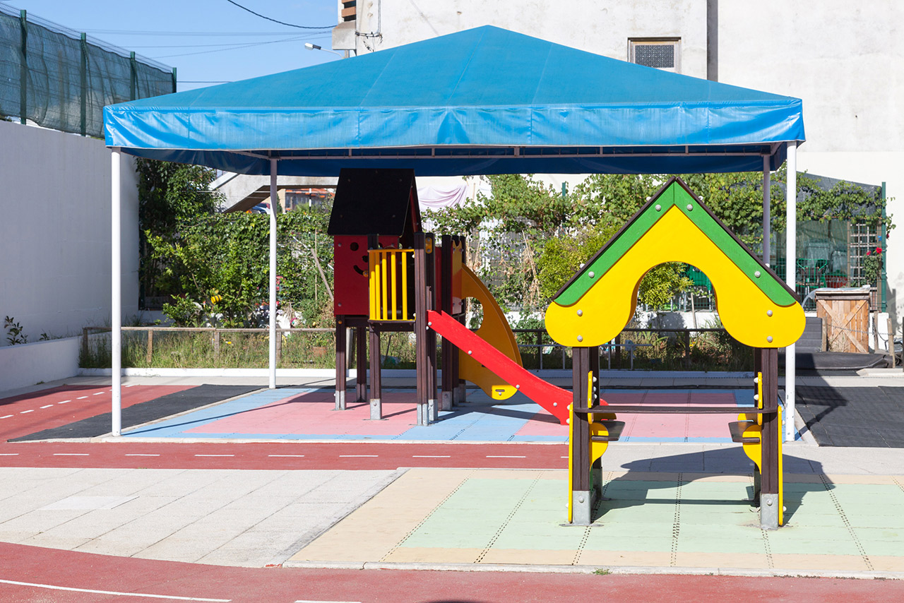 Preschool playground with colorful play structures under a blue canopy