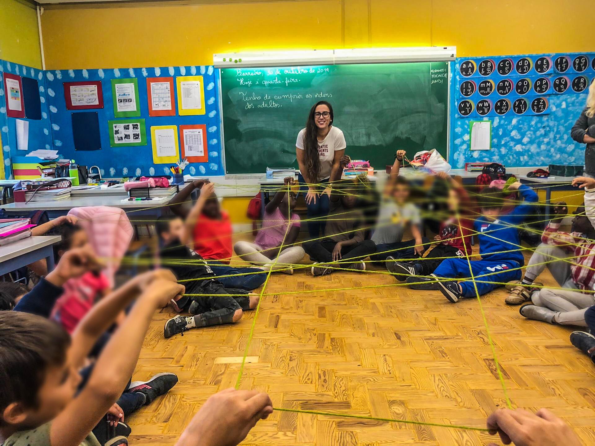 Preschool children participate in a collaborative classroom activity, working together to navigate a complex web of string.