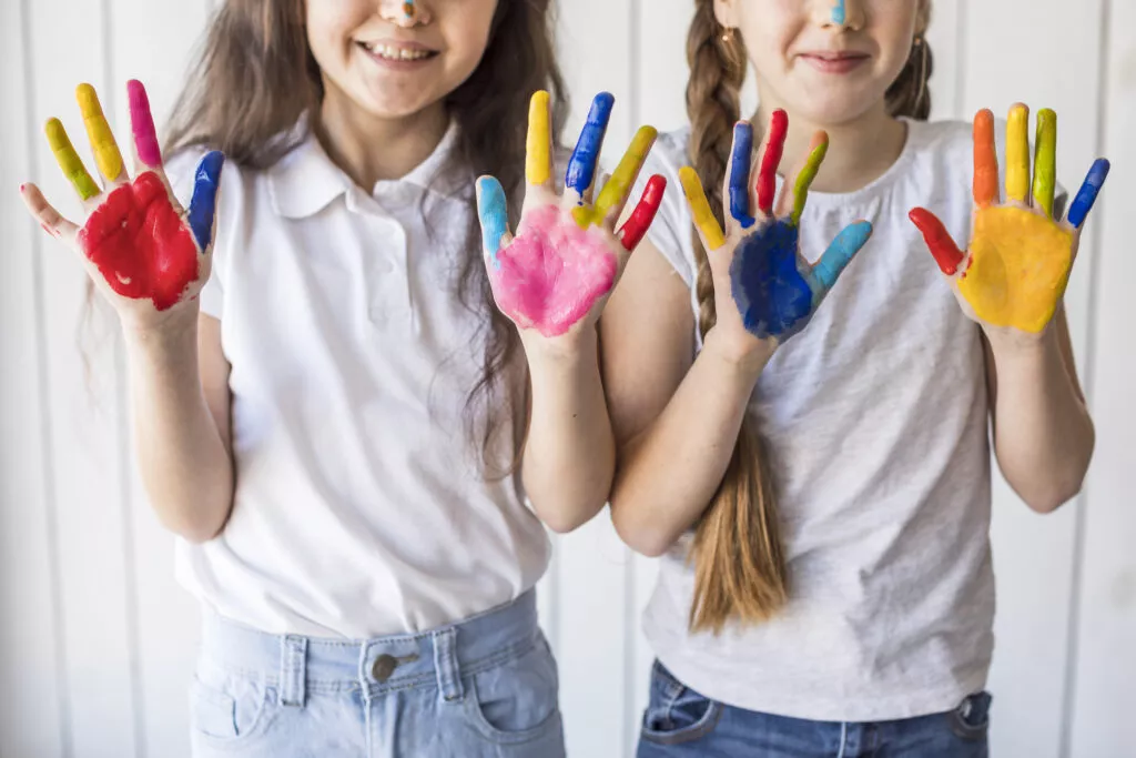 Two smiling preschool girls proudly displaying their colorful handprints