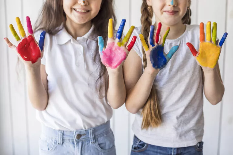 Two smiling preschool girls proudly displaying their colorful handprints