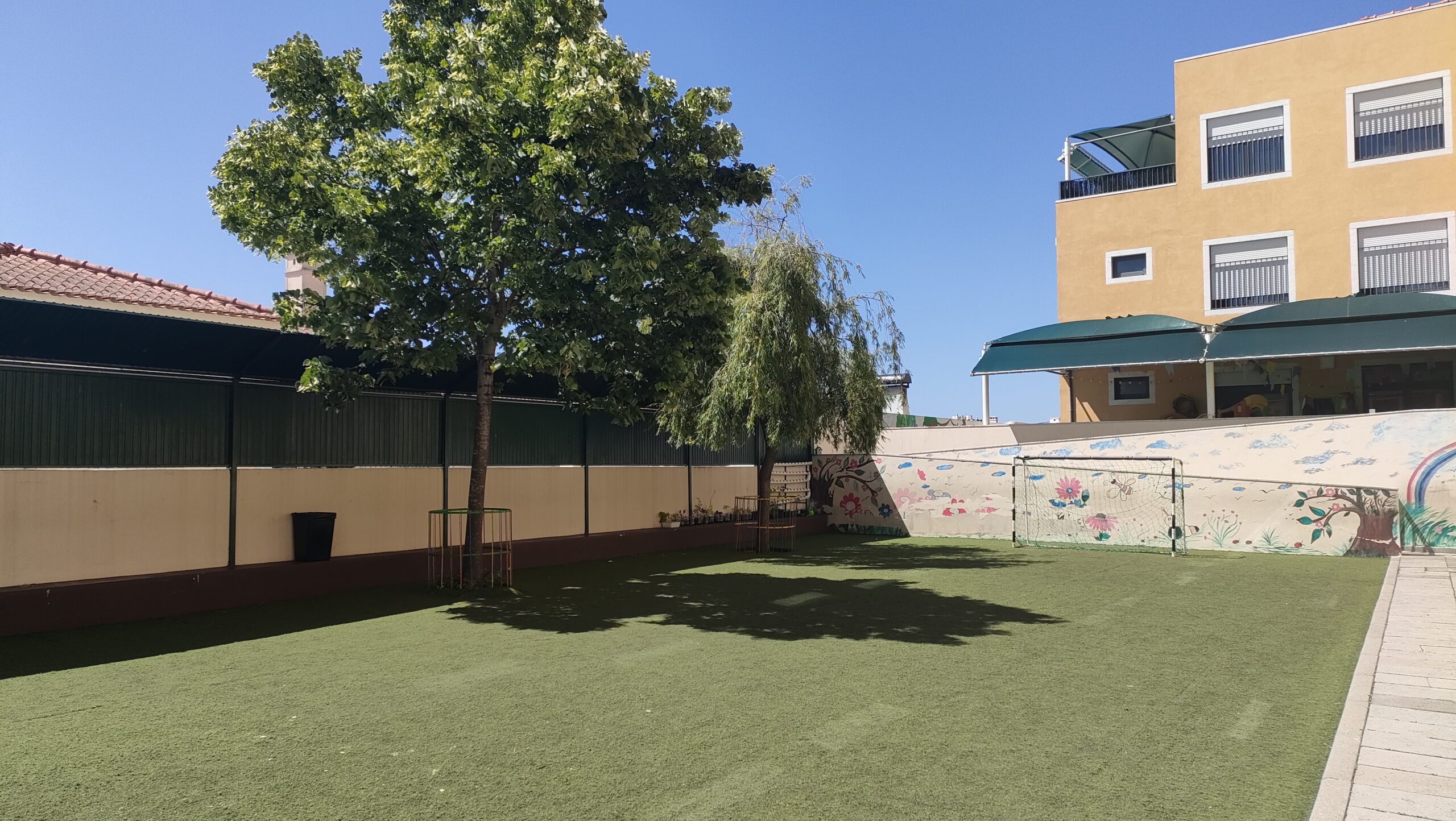 Preschool playground with artificial turf, trees, and a painted wall mural