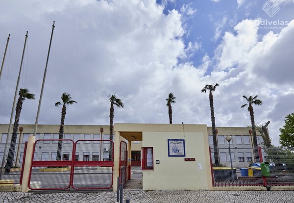 Exterior view of the school building, showing the entrance gate and palm trees.