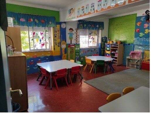 Preschool classroom with colorful tables and chairs, and educational wall decorations.
