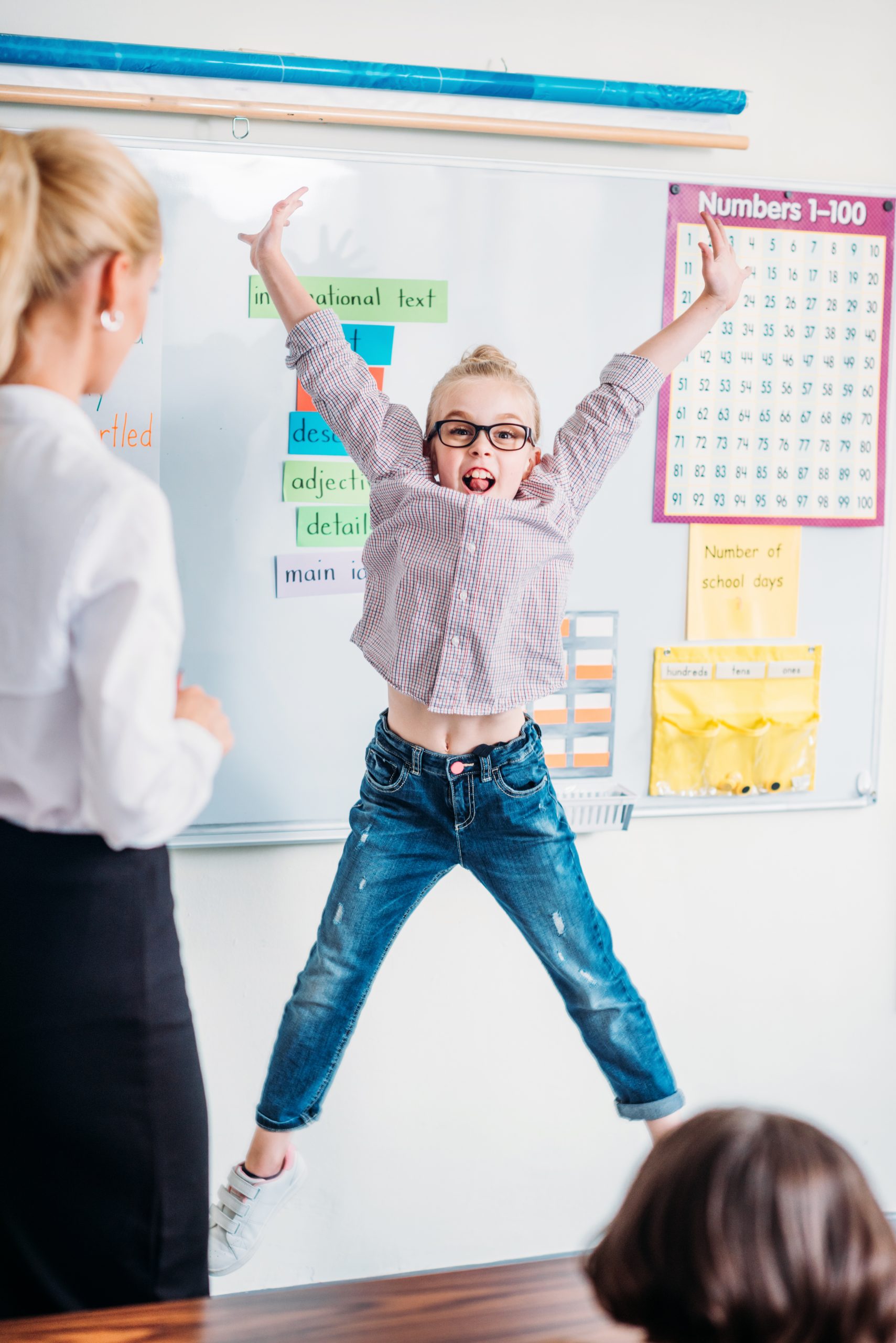 Preschool student joyfully raising her hands in a classroom setting