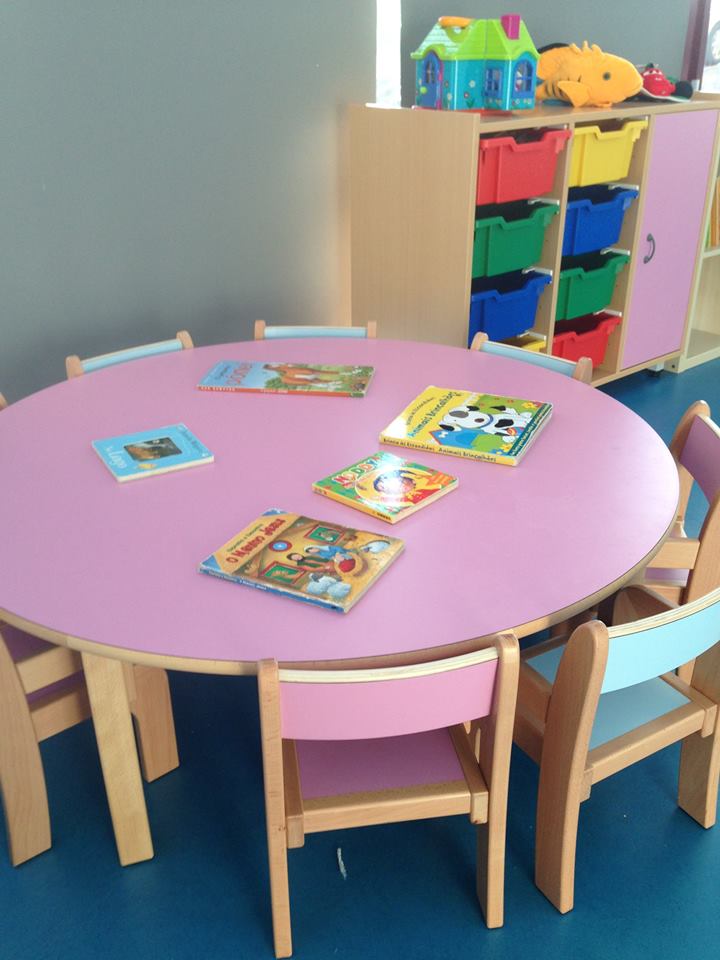 Preschool classroom with a pink table and chairs, surrounded by colorful storage units and children's books.