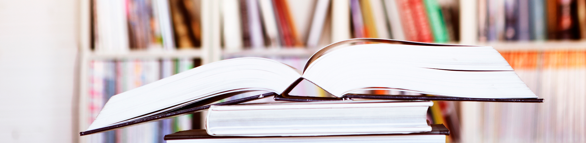 Open book on a stack of books in front of a blurry bookshelf