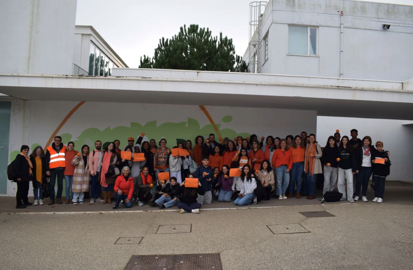 Group photo of students, teachers, and staff at Agrupamento de Escolas Lima de Freitas holding oranges