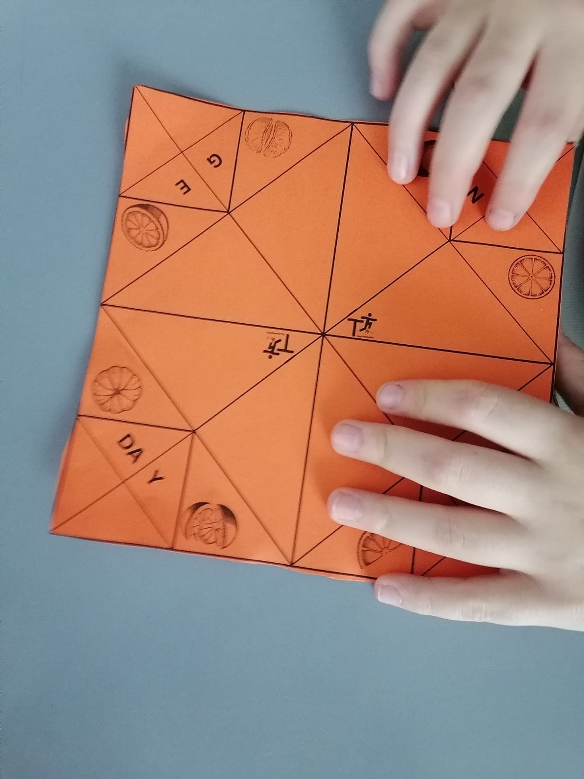 Student hands working on an orange paper game