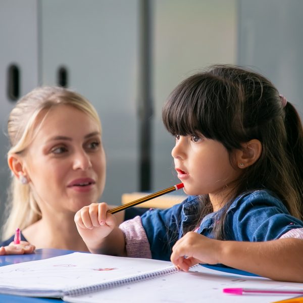 Preschool teacher assisting a student with writing and reading activities