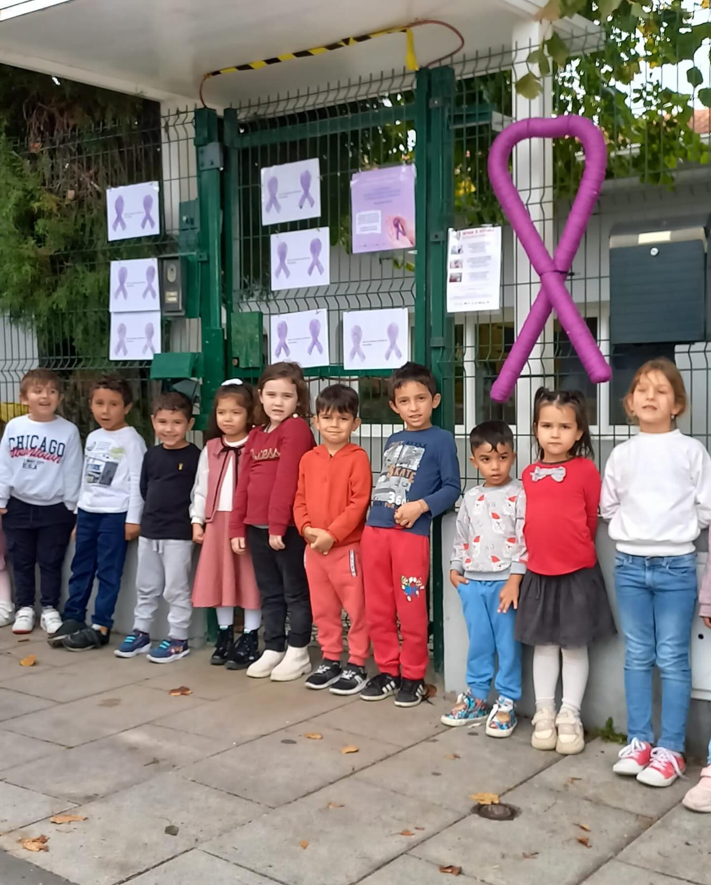 Preschool children standing in front of a fence with purple ribbons