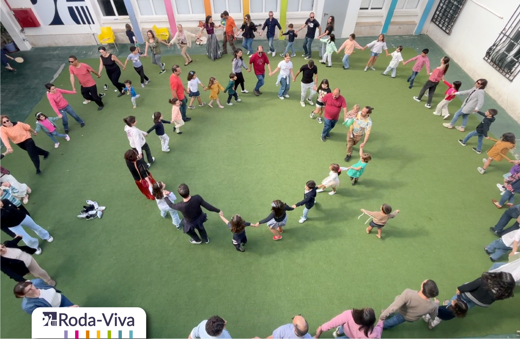 Children and adults holding hands in a circle during an outdoor school event at Academy Luísa Todi.
