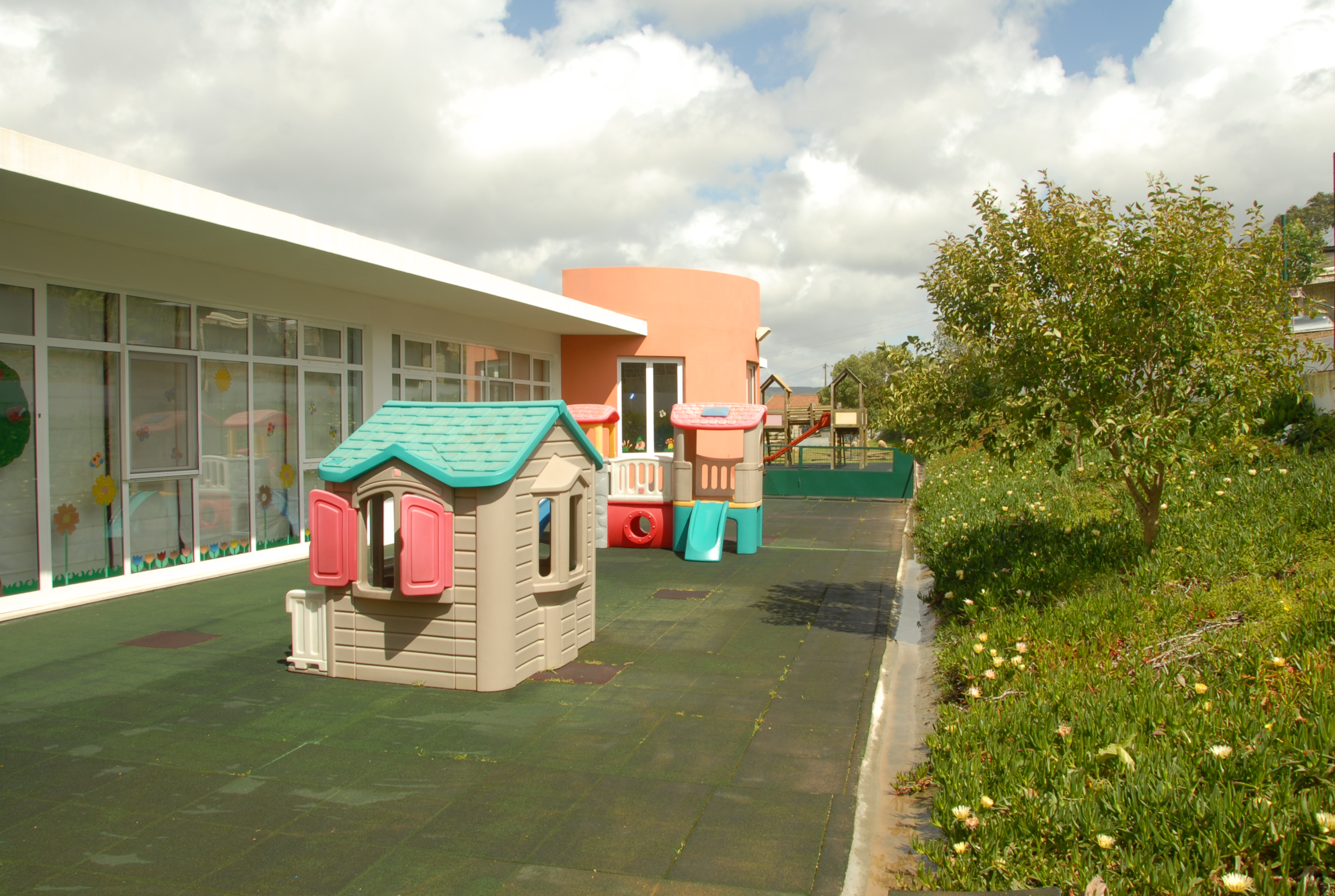 Preschool playground with colorful plastic playhouses and a green rubber surface.