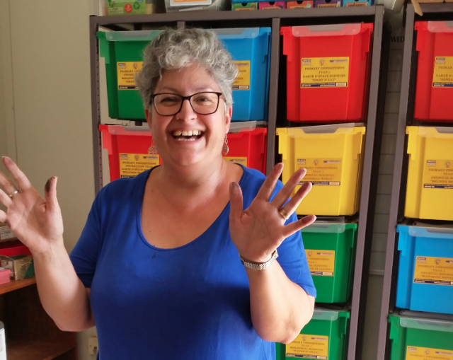 Happy teacher showing her hands with paint, in a classroom with colorful bins