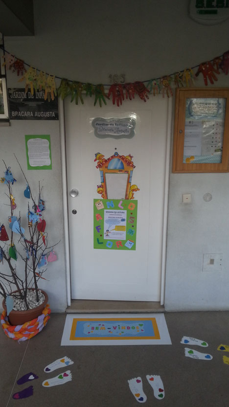 Preschool entrance decorated with colorful handprints, welcome mat, and children's artwork