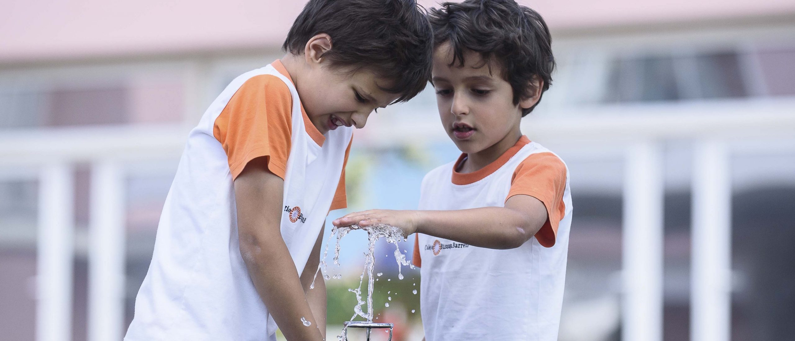 Two students in uniform playing with water fountain at Colégio Bissaya Barreto