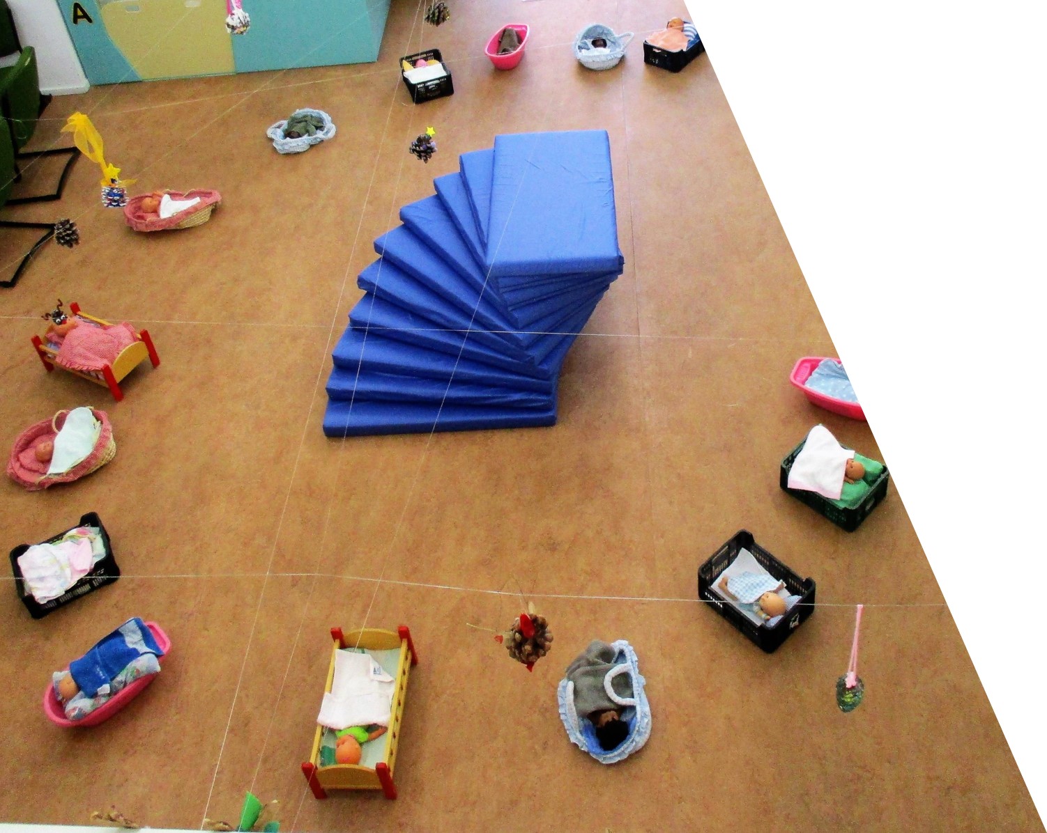 Preschool classroom with baby dolls in beds and cribs, and a blue mat on the floor.