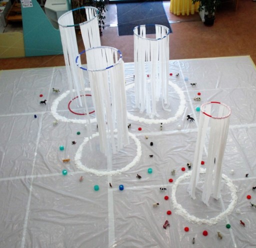 Preschool children's art installation with white fabric hanging from hoops and small toy animals arranged on the floor