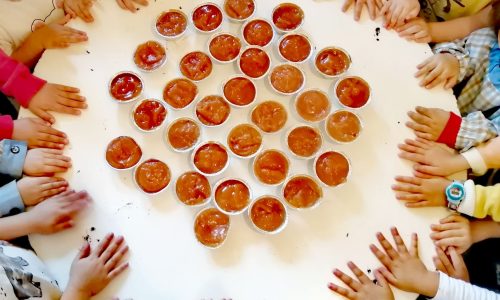 Preschool children gathered around a table with small cups of food, likely participating in a class activity or snack time.