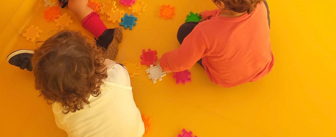 Preschool children playing with colorful blocks on a yellow floor