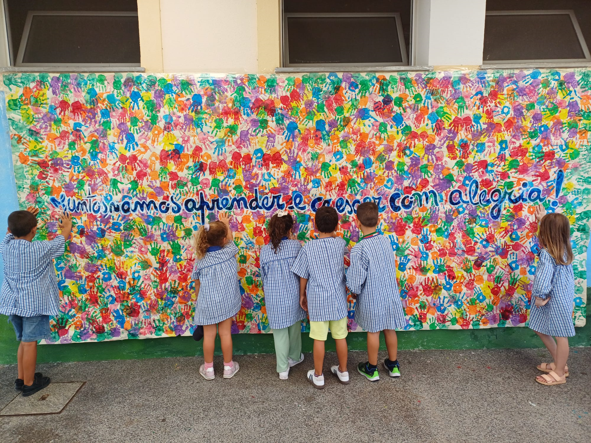 Preschool students admire a colorful handprint mural.
