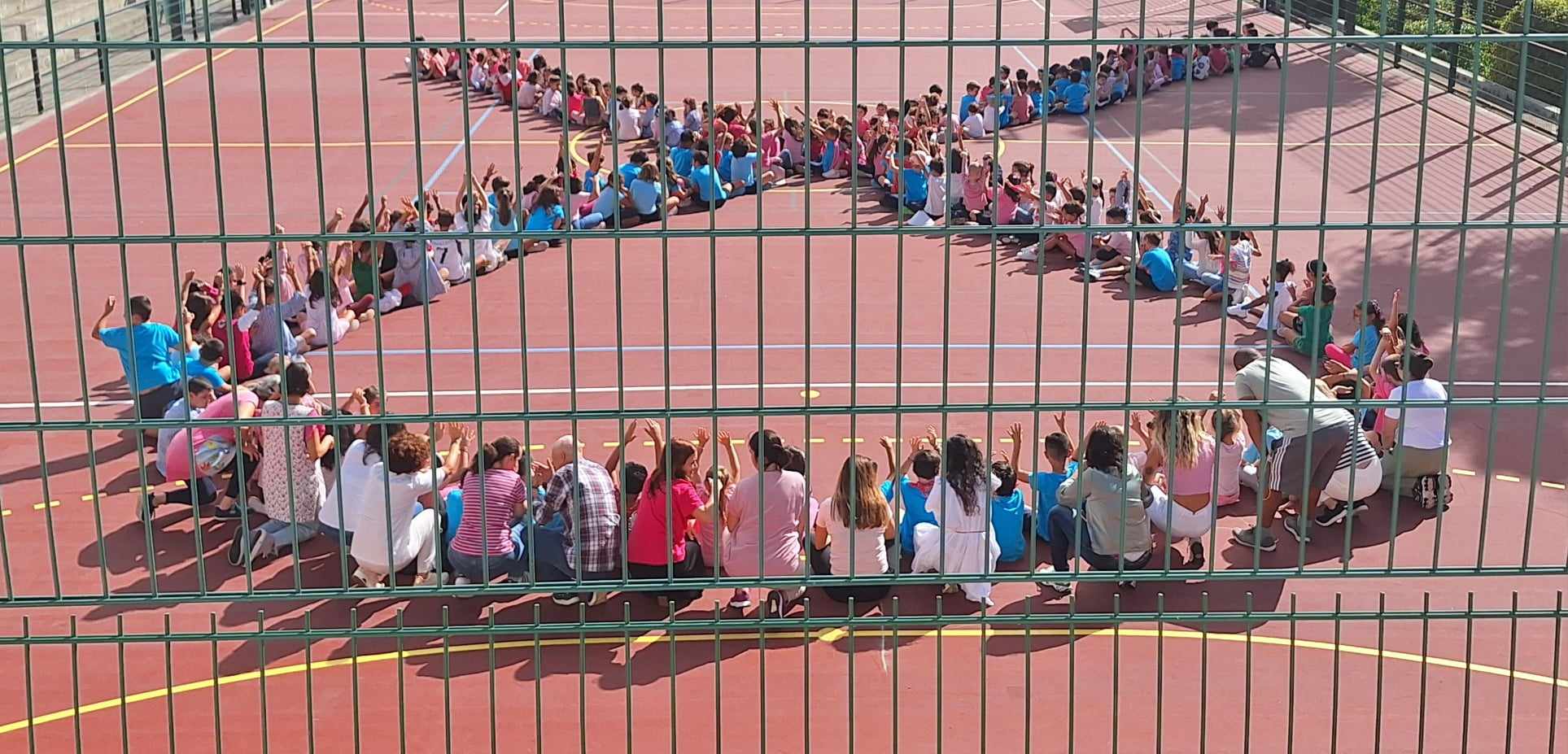Students and teachers forming a pink ribbon shape on the playground, symbolizing breast cancer awareness.