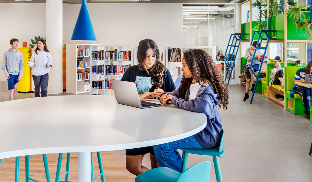 Two students working together on a laptop in a modern school library