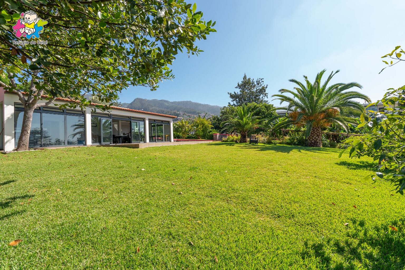 Refúgio do Bebé preschool building with large windows and a spacious green lawn