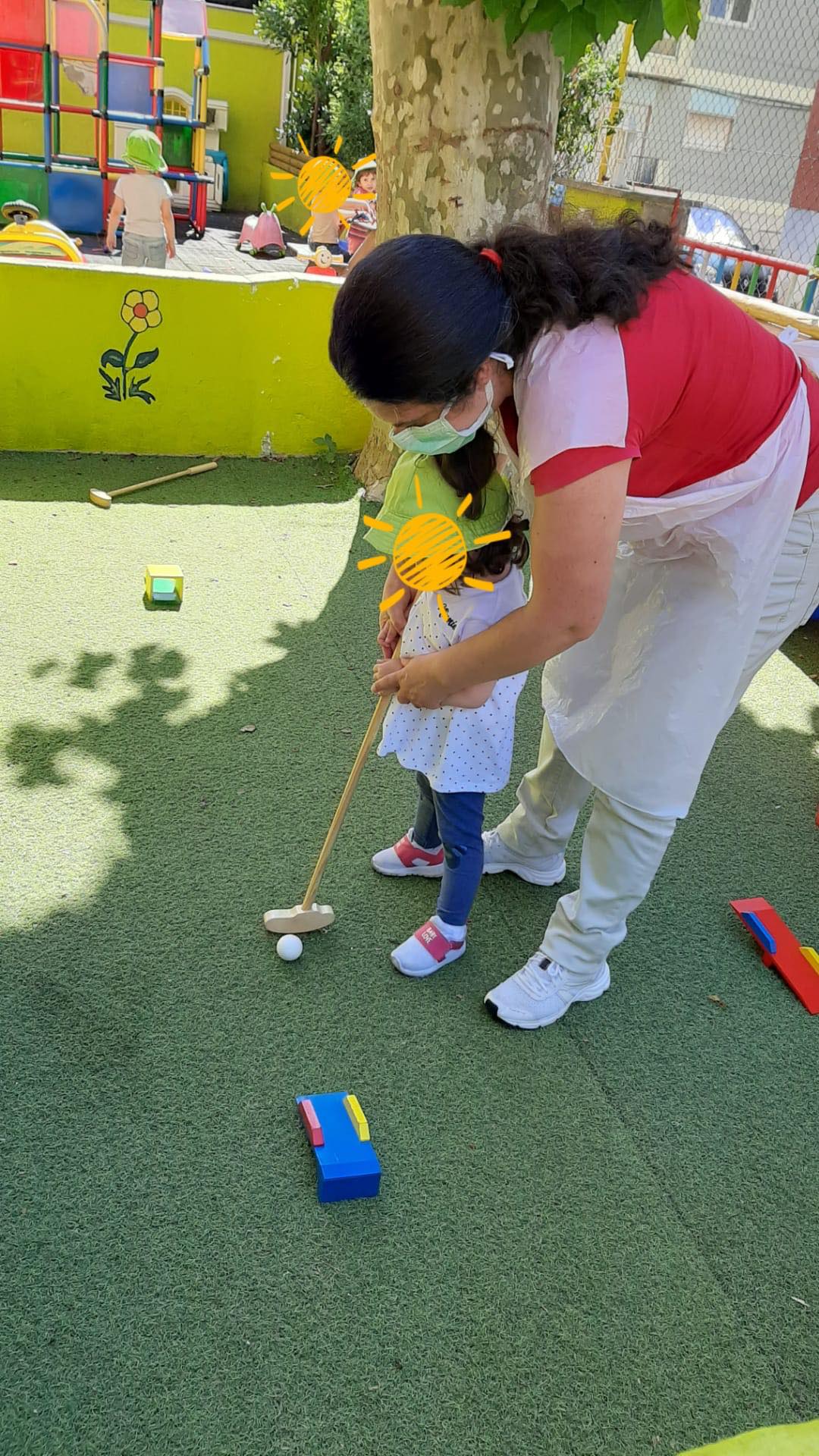 Preschool teacher assisting a child with mini golf
