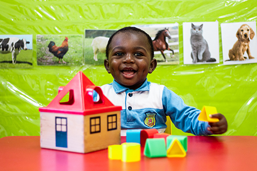 Happy preschool student playing with blocks and a toy house