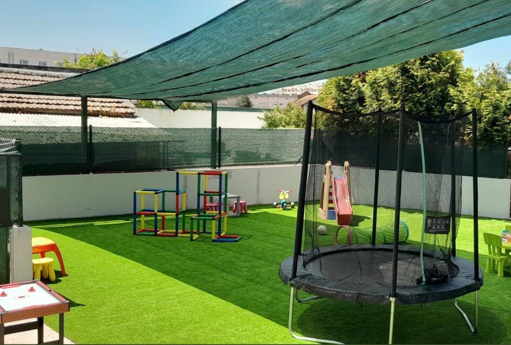 Preschool playground with colorful play structures, a trampoline, and artificial turf.