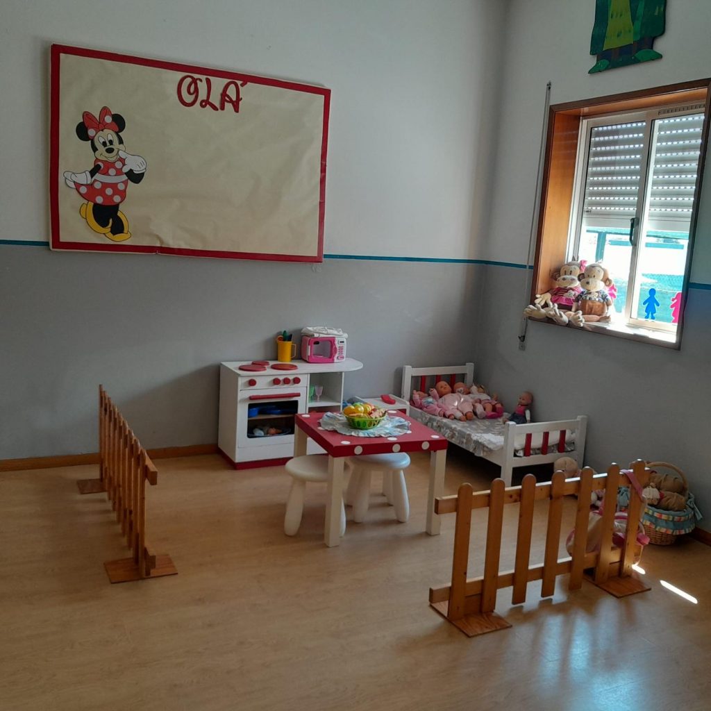 Preschool classroom play area with toy kitchen, table, and dolls