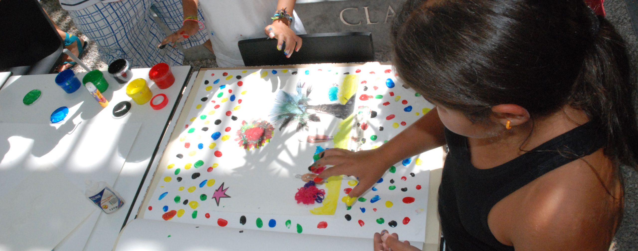 Preschool children participate in a collaborative art project, painting colorful dots on a large piece of paper.