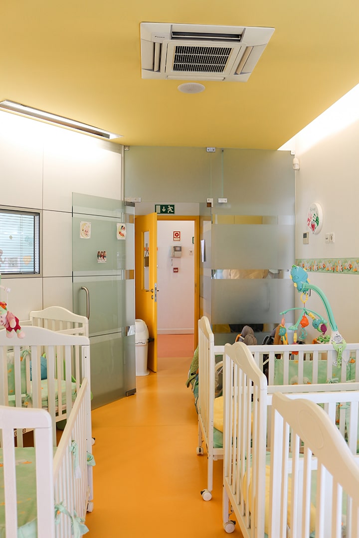 Nursery room at A Patatina preschool with multiple cribs and a bright yellow floor