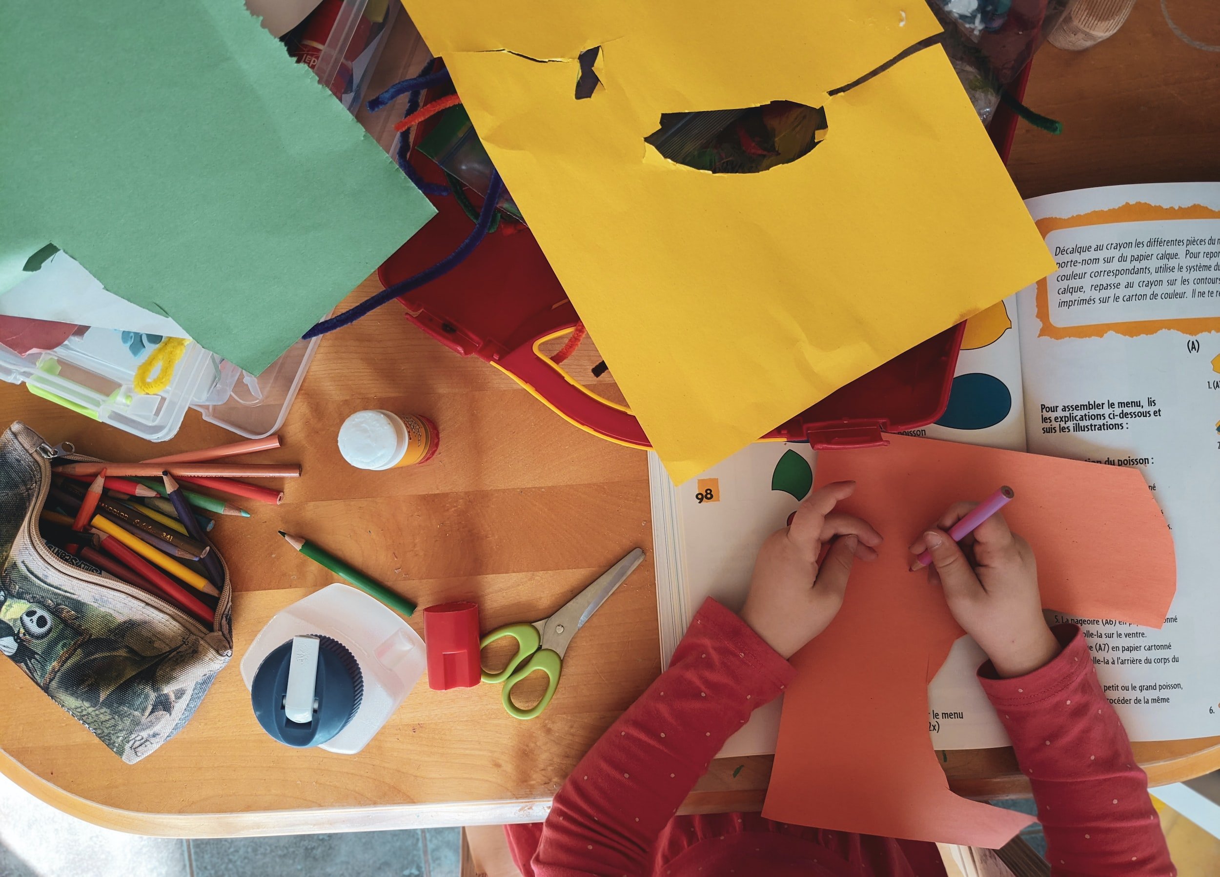 Preschool child working on a craft project at a table.  Colored pencils, scissors, and construction paper are visible.
