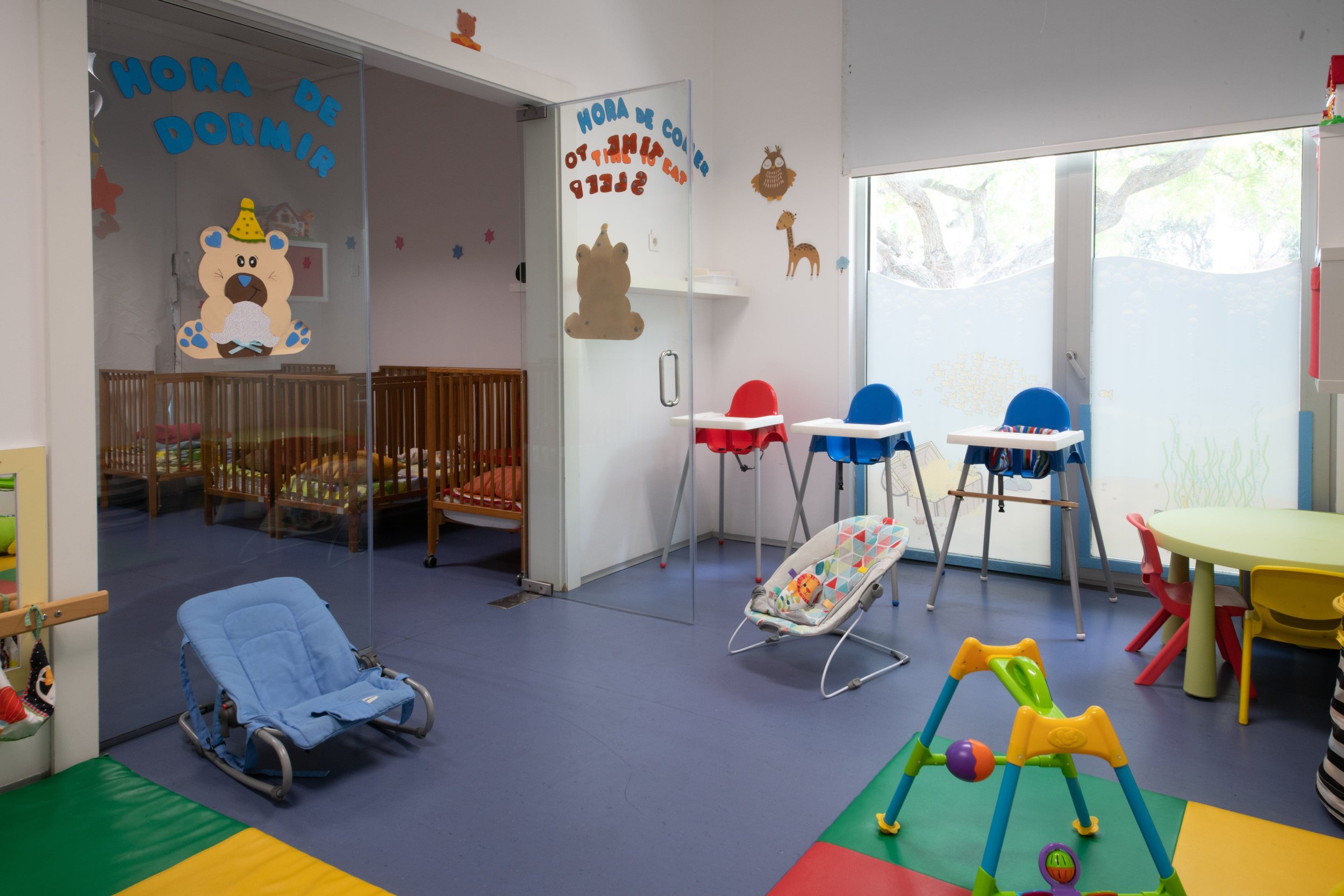 Preschool classroom with cribs, high chairs, and play equipment