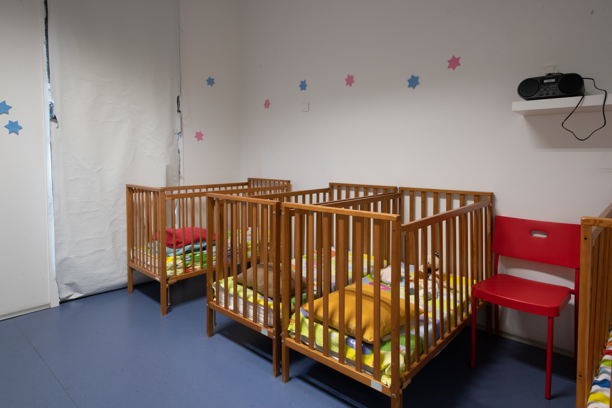 Wooden cribs with colorful bedding in a nursery at Saídos da Casca - Berçário e Creche preschool.