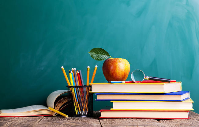 Books, pencils, and an apple on a desk in front of a chalkboard