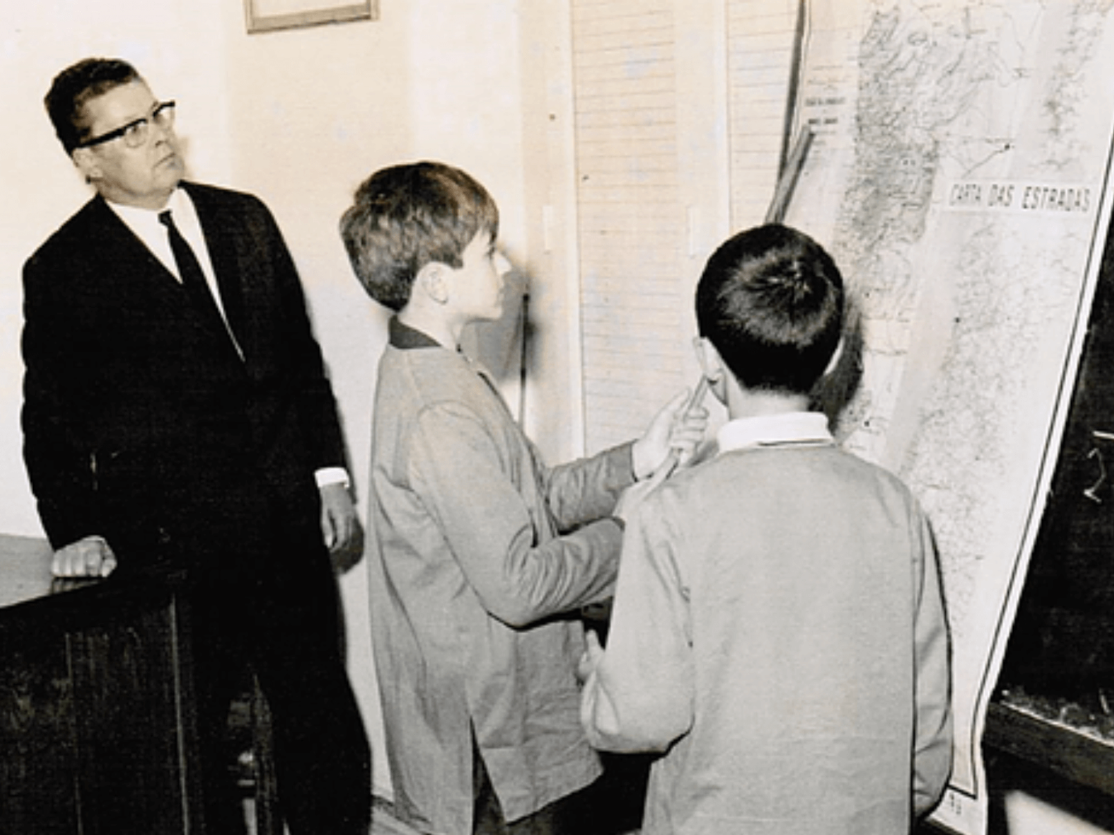 Black and white photo of a teacher and two students studying a map
